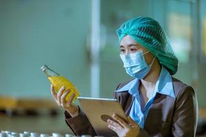 Worker of science in bottle beverage factory wearing safety hat posing show work to check quality of Basil seed produce on conveyer belt before distribution to market business. photo