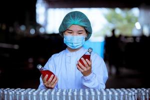 trabajador científico en una fábrica de bebidas embotelladas con sombrero de seguridad posando para comprobar la calidad de los productos de semillas de albahaca en la cinta transportadora antes de su distribución al negocio del mercado. foto