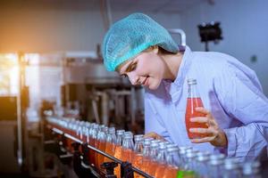 trabajador científico en una fábrica de bebidas embotelladas con sombrero de seguridad posando para comprobar la calidad de los productos de semillas de albahaca en la cinta transportadora antes de su distribución al negocio del mercado. foto