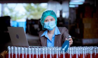 trabajador científico en una fábrica de bebidas embotelladas con sombrero de seguridad posando para comprobar la calidad de los productos de semillas de albahaca en la cinta transportadora antes de su distribución al negocio del mercado. foto