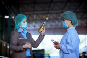 Worker of science in bottle beverage factory wearing safety hat posing show work to check quality of Basil seed produce on conveyer belt before distribution to market business. photo