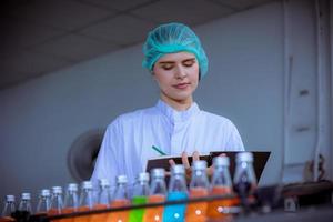 Worker of science in bottle beverage factory wearing safety hat posing show work to check quality of Basil seed produce on conveyer belt before distribution to market business. photo