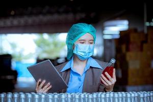 Worker of science in bottle beverage factory wearing safety hat posing show work to check quality of Basil seed produce on conveyer belt before distribution to market business. photo