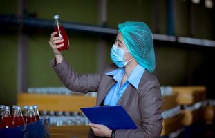 trabajador científico en una fábrica de bebidas embotelladas con sombrero de seguridad posando para comprobar la calidad de los productos de semillas de albahaca en la cinta transportadora antes de su distribución al negocio del mercado. foto