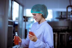 Worker of science in bottle beverage factory wearing safety hat posing show work to check quality of Basil seed produce on conveyer belt before distribution to market business. photo