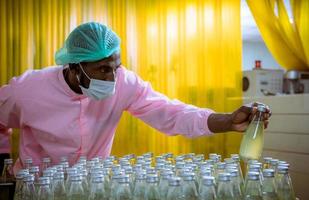 trabajador científico en una fábrica de bebidas embotelladas con sombrero de seguridad posando para comprobar la calidad de los productos de semillas de albahaca en la cinta transportadora antes de su distribución al negocio del mercado. foto