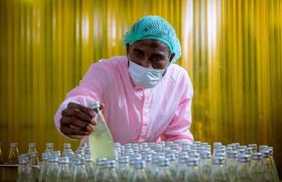 Worker of science in bottle beverage factory wearing safety hat posing show work to check quality of Basil seed produce on conveyer belt before distribution to market business. photo