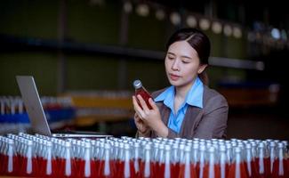 Worker of science in bottle beverage factory wearing safety hat posing show work to check quality of Basil seed produce on conveyer belt before distribution to market business. photo