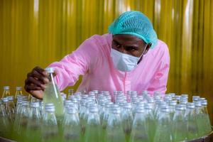 trabajador científico en una fábrica de bebidas embotelladas con sombrero de seguridad posando para comprobar la calidad de los productos de semillas de albahaca en la cinta transportadora antes de su distribución al negocio del mercado. foto