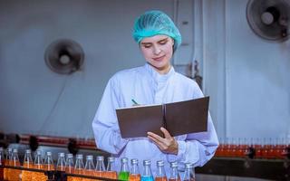 trabajador científico en una fábrica de bebidas embotelladas con sombrero de seguridad posando para comprobar la calidad de los productos de semillas de albahaca en la cinta transportadora antes de su distribución al negocio del mercado. foto