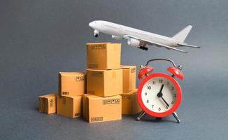 Cargo plane, stack of cardboard boxes and a red alarm clock. Express air delivery concept. Temporary storage, limited offer and discount. Optimization of logistics, improving efficiency photo