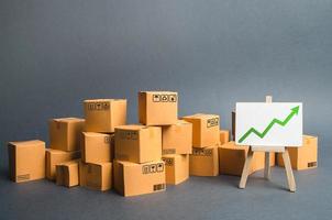 Lots of cardboard boxes and a stand with a green up arrow. rate growth of production of goods and products, increasing economic indicators. Increasing consumer demand, increasing exports or imports. photo