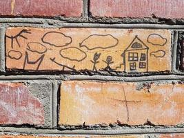 Cute children's drawing with a felt-tip pen on a red brick wall. Clouds, sun, home and family. photo