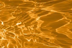 desenfoque borrosa transparente de color dorado claro textura de la superficie del agua tranquila con salpicaduras y burbujas. fondo de naturaleza abstracta de moda. ondas de agua a la luz del sol con espacio de copia. brillo de acuarela amarilla foto