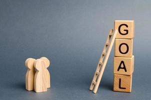 Three people are standing near the tower of cubes with the word goal. Evaluation of options and means to conquer the summit and achieve the goal. Business concept. cooperation and teamwork photo