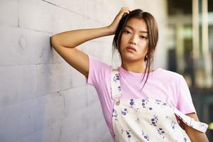 Attractive Chinese girl looking at camera with serious expression leaning against an urban wall photo