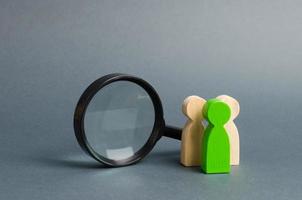 Three wooden human figure stands near a magnifying glass on a gray background. The concept of the search for people and workers. Search for vacancies and work. Human resources, management. photo