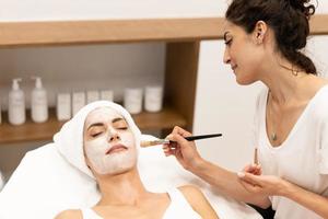 Aesthetics applying a mask to the face of a Middle-aged woman in modern wellness center. photo