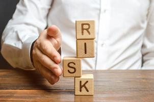 A man straightens a segment in an unstable tower of cubes labeled Risk. Risk management, cost assessment, and business and investment safety. Strengthen business resilience and flexibility. photo
