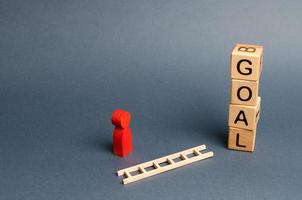 tower of cubes with an inscription goal and a red figure of a man stands near fallen ladder. concept of achieving the goal, subject to the application of all the efforts and desires. Tool for success. photo