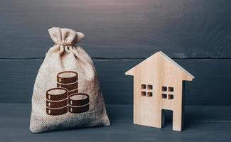 Wooden house and cash coins money bag. Buying and selling real estate. Taxes. Mortgage loan. Sale of housing. Proposal for a deal price. First installment. Maintenance, property improvement. photo