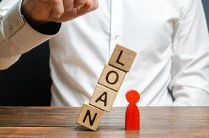 Man pushes downs a cube tower with the word Loan on the red man figure. Lack of protection for vulnerable groups of the population. Debt pit. Harassment of the borrower by collectors. Threat of life photo