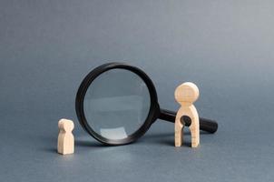 A wooden figure of a woman with emptiness and a child stands near the magnifying glass. The concept of finding a child, the adoption of children. Mother lost her baby and is now looking for him. photo