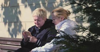 Zwei Mädchen sitzen an einem sonnigen Herbsttag auf einer Bank in der Nähe des Schwarzmeerdamms und schauen auf das Telefon video