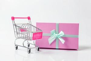 carrito de supermercado pequeño para comprar juguetes con caja de regalo rosa aislada en fondo blanco. venta comprar centro comercial mercado tienda consumidor concepto. copie el espacio foto