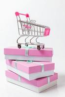 Small supermarket grocery push cart for shopping toy with pink gift box isolated on white background. Sale buy mall market shop consumer concept. Copy space. photo
