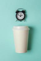 Simply flat lay design paper coffee cup and alarm clock on blue pastel colorful trendy background. Takeaway drink and breakfast beverage. Good morning wake up awake concept. Top view copy space. photo