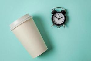 Simply flat lay design paper coffee cup and alarm clock on blue pastel colorful trendy background. Takeaway drink and breakfast beverage. Good morning wake up awake concept. Top view copy space. photo