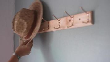 Close up of woman hand put straw hat on clothes hanger in living room video