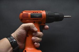 Orange screwdriver on a black background in the hand. Screwdriver and electric drill with power supply photo