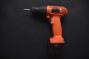 Orange screwdriver on a black background in the hand. Screwdriver and electric drill with power supply photo