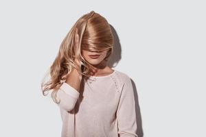 Feeling free to do anything. Beautiful young woman covering face with hair and smiling while standing against grey background photo