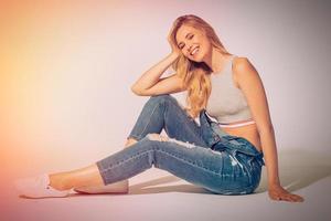 belleza despreocupada. foto de estudio de una hermosa joven en jeans en general mirando a la cámara y sonriendo mientras se sienta en el suelo