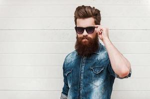 Rugged and manly. Confident young bearded man looking at camera and adjusting eyewear while standing outdoors photo