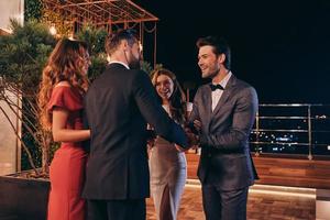 Group of people in formalwear communicating and smiling while spending time on luxury party photo