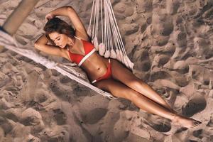 Summer relaxation. Full length top view of attractive young woman in swimwear keeping hands behind head while lying down in hammock outdoors photo