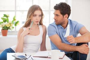 You spend too much money. Angry young man showing a bill to his wife while both sitting on the floor at his apartment photo