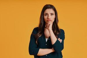 Sad young woman in casual clothing making a face while standing against yellow background photo