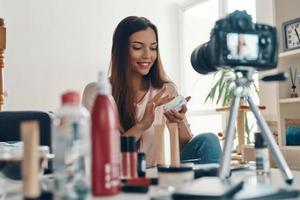 Happy young woman applying lip gloss and smiling while making social media video photo