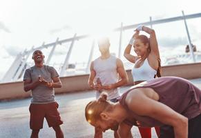 Group of young people in sports clothing smiling while exercising outdoors photo