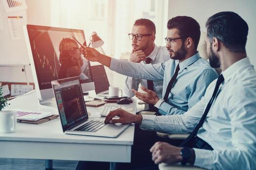 Considering the next step. Group of young modern men in formalwear analyzing stock market data while working in the office photo