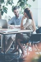 Discussing business. Two young business people in smart casual wear discussing something while sitting at the office desk together photo