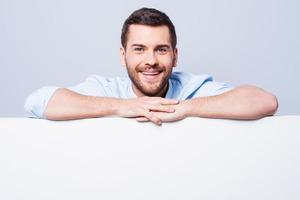 Leaning at the copy space. Handsome young man leaning at copy space while standing against grey background photo