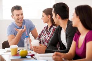 Students meeting. Four cheerful students talking to each other while sitting at the desk photo