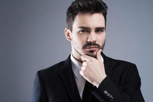 Confident and handsome. Portrait of confident young man in formalwear looking at camera while standing against grey background photo