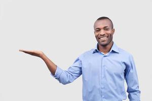 Holding a copy space. Cheerful young African man holding a copy space and smiling while standing isolated on grey background photo